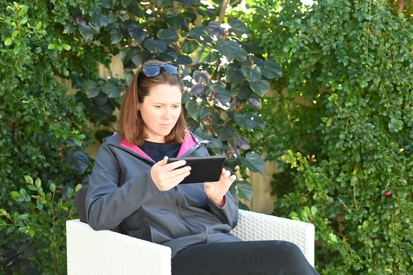 松懈的成年女性 40岁 在家后花园阅读或观看平板电脑视频 — 图库照片
