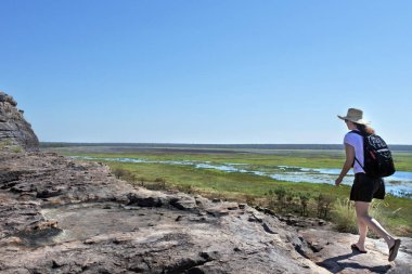 Avustralya 'nın kuzeyindeki Kakadu Ulusal Parkı manzarası karşısında Ubirr Kayası' nda yürüyüş yapan Avustralyalı yetişkin kadın turist..