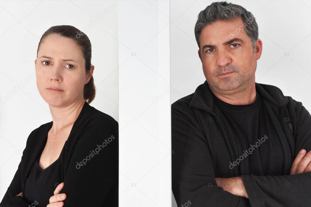 Upset adult couple age 30-40 having a fight at home leaning on a separation wall looking at camera.