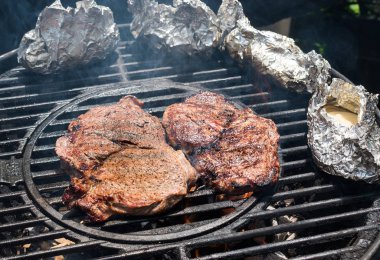 Ateşte folyo yanlarıyla yuvarlak ızgarada iki biftek