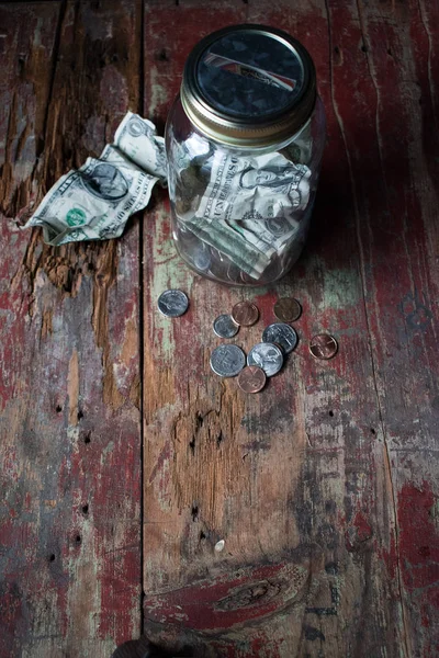 Money jar with dollars and change on old wooden table