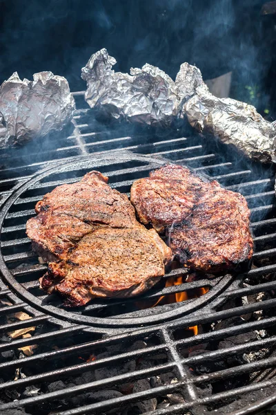 Two steaks on round grill with tinfoil sides over fire