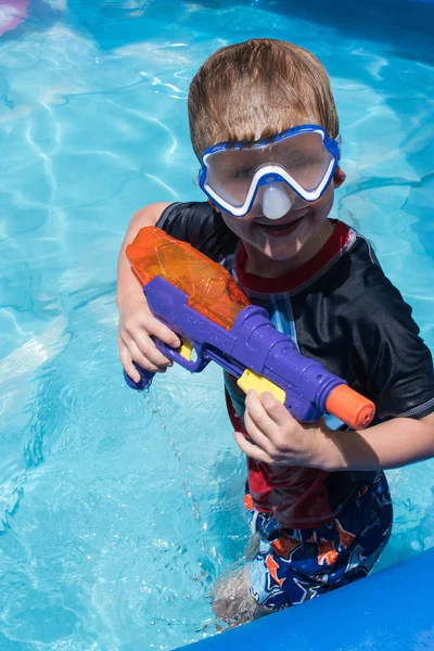 young boy with water gun and goggles in pool