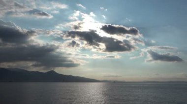 Yumuşak bulutların yavaşça solan güneşe doğru hareket ettiğini gösteriyor. Güneş 'in altın-turuncu ışınları okyanusa yansıyor.