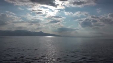 Yumuşak bulutların yavaşça solan güneşe doğru hareket ettiğini gösteriyor. Güneş 'in altın-turuncu ışınları okyanusa yansıyor.