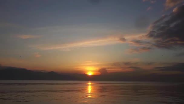 日没の静かな島 薄日に向かってゆっくりと動くふわふわの雲を見せてくれます 太陽の黄金のオレンジ色の光線は 完全に穏やかな海に反射されます — ストック動画