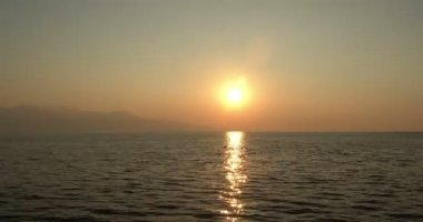 Gün batımında sessiz bir ada. Yumuşak bulutların yavaşça solan güneşe doğru hareket ettiğini gösteriyor. Güneş 'in altın-turuncu ışınları okyanusa yansıyor..