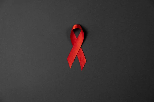 Widok z góry na świadomość czerwonej wstążki na szarym tle stołu dla kampanii World Aids Day. Płaskie ułożenie, przestrzeń kopiowania — Zdjęcie stockowe