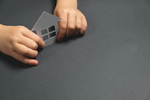 Nahaufnahme horizontales Bild der Kinderhände, die weißes Papierhaus auf grauem Hintergrund halten. Familienheim und Immobilienkonzept. flache Lage, Kopierraum — Stockfoto