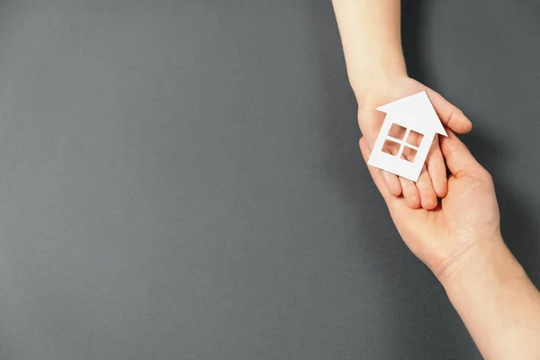 Visão superior em mãos femininas e infantis segurando a casa de papel branco no fundo cinza. Casa de família e conceito imobiliário. Flat lay, espaço de cópia — Fotografia de Stock