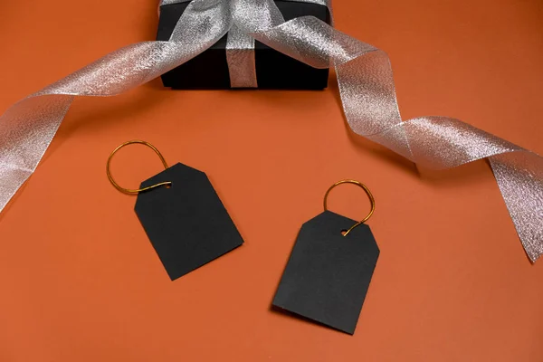 Coffret cadeau enveloppé dans du papier noir avec ruban argenté et étiquettes de prix sur fond orange vif. Copier l'espace et la vue du dessus. Cadeau cadeau boîte vendredi noir isolé . — Photo