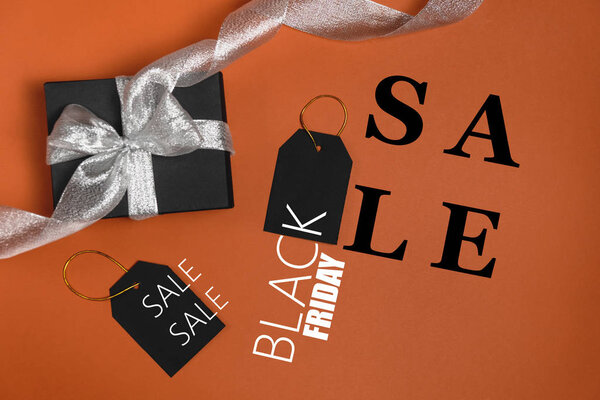 Black friday sale concept. Black paper boxes with silver ribbon, price tags and text on bright orange background. Flat lay, top view, copy space