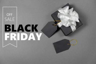 Gümüş kurdele fiyat etiketli siyah kağıda sarılı hediye kutusu ve parlak gri arka planda metin. Boşluğu ve üst görünümü kopyala. Kara Cuma Kutusu hediyesi izole edilmiş..