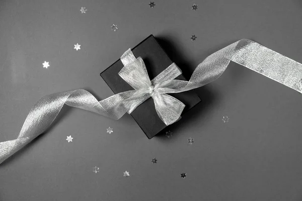 Coffret cadeau enveloppé dans du papier noir avec ruban argenté, étoiles confettis et étiquettes de prix sur fond gris. Copier l'espace et la vue du dessus. Cadeau cadeau boîte vendredi noir isolé . — Photo