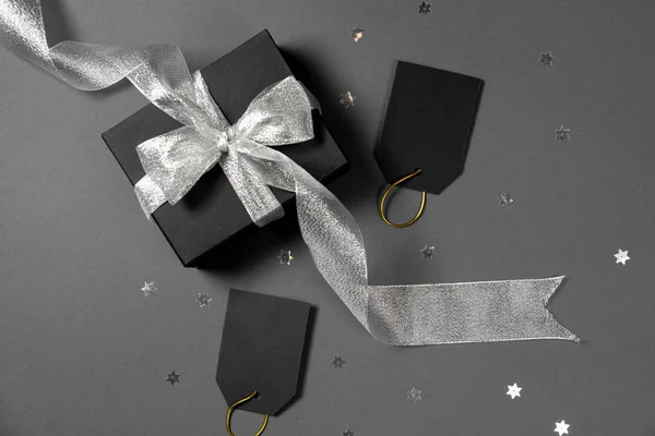 Caja de regalo envuelta en papel negro con cinta plateada, estrellas confeti y etiquetas de precio sobre fondo gris brillante. Copiar espacio y vista superior. Viernes negro caja regalo regalo aislado . — Foto de Stock