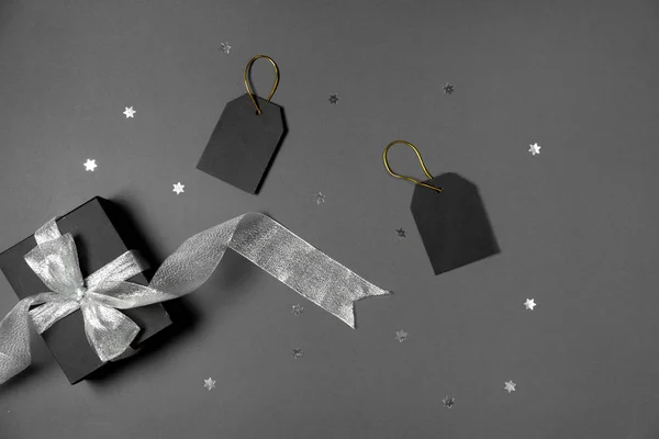 Caja de regalo envuelta en papel negro con cinta plateada, estrellas confeti y etiquetas de precios sobre fondo gris. Copiar espacio y vista superior. Viernes negro caja regalo regalo aislado . — Foto de Stock