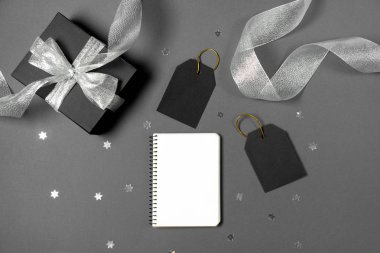 Gümüş kurdele, defter, yıldız konfetileri ve gri arka planda fiyat etiketleriyle siyah kağıda sarılı hediye kutusu. Boşluğu ve üst görünümü kopyala. Kara Cuma Kutusu hediyesi izole edilmiş..