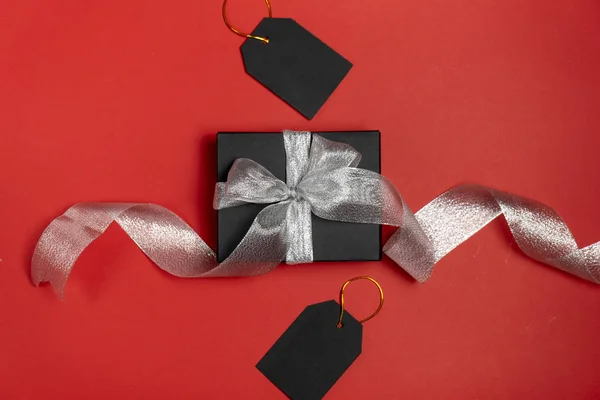 Geschenkverpackung in schwarzem Papier mit silbernem Band und Preisschildern auf leuchtend rotem Hintergrund. Kopierraum und Draufsicht. Black Friday Box Geschenk Geschenk isoliert. — Stockfoto