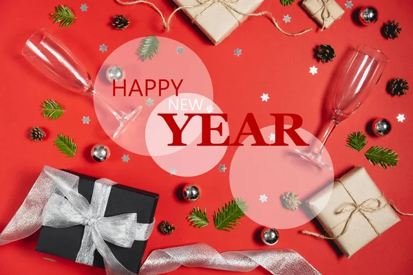 С Новым годом, рождественская безделушка с ручной работы подарочные коробки украшены бумагой из ветвей елки, два бокала шампанского, сосны и конфетти на красном фоне. Плоская кладка, вид сверху, копировальное пространство — стоковое фото