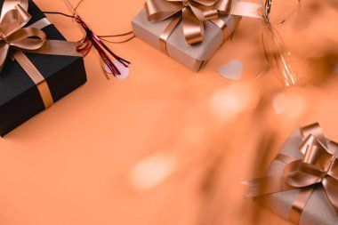 Tatil geçmişi. Turuncu arka planda pembe kalp konfetisiyle süslenmiş çeşitli el yapımı hediye kutuları. Minimal tarz ve sevgililer günü konsepti. Düz konum, üst görünüm, kopyalama alanı