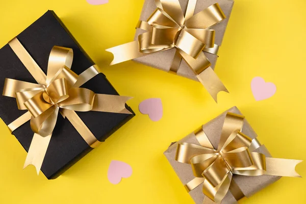 Fondo de vacaciones. Varias cajas de regalo hechas a mano decoradas con confeti rosa sobre fondo amarillo. Estilo mínimo y concepto de día de San Valentín. Plano, vista superior, espacio para copiar — Foto de Stock