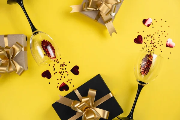 Valentijnsdag achtergrond. Twee klinkende wijnglazen, verschillende handgemaakte geschenkdozen versierd met rode hart confetti op gele achtergrond. Valentijnsdag concept. Vlakke lay, bovenaanzicht, kopieerruimte — Stockfoto