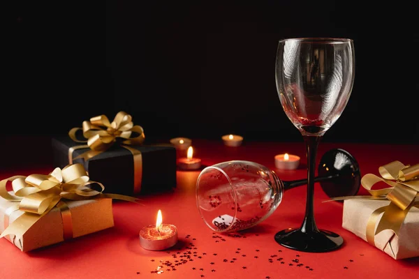 Valentijnsdag achtergrond. Twee klinkende wijnglazen, verschillende handgemaakte geschenkdozen versierd met confetti, kaars op rode en zwarte achtergrond. Valentijnsdag concept. Vlakke lay, kopieerruimte — Stockfoto