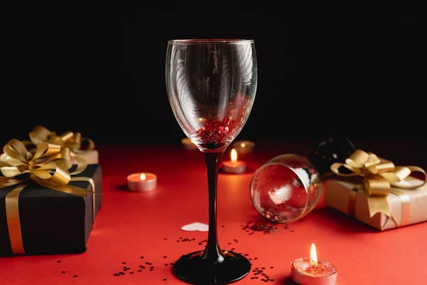 Vakantie achtergrond. Twee klinkende wijnglazen, verschillende handgemaakte geschenkdozen versierd met confetti, kaars op rode en zwarte achtergrond. Valentijnsdag concept. Vlakke lay, kopieerruimte — Stockfoto