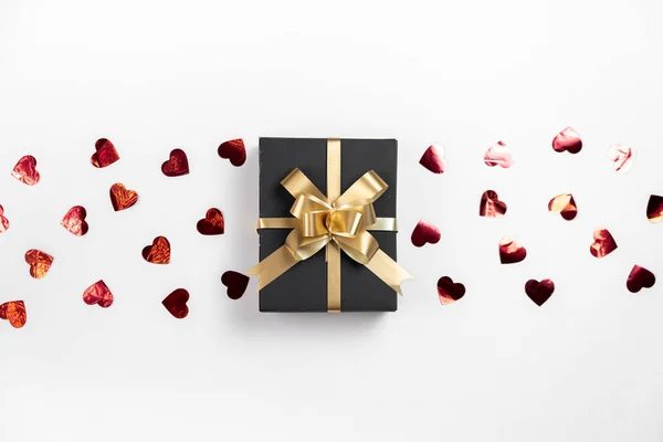 Fondo del Día de San Valentín. Caja de regalo hecha a mano decorada con confeti corazón rojo sobre fondo blanco. Estilo mínimo y concepto de día de San Valentín. Plano, vista superior, espacio para copiar — Foto de Stock