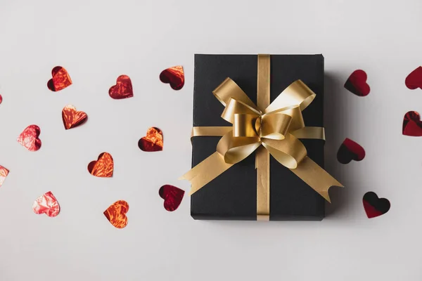 Nyaralási háttér. Kézzel készített ajándék doboz díszített piros szív konfetti szürke alapon. Minimális stílus és Valentin napi koncepció. Lapos fekvés, felülnézet, másolás — Stock Fotó