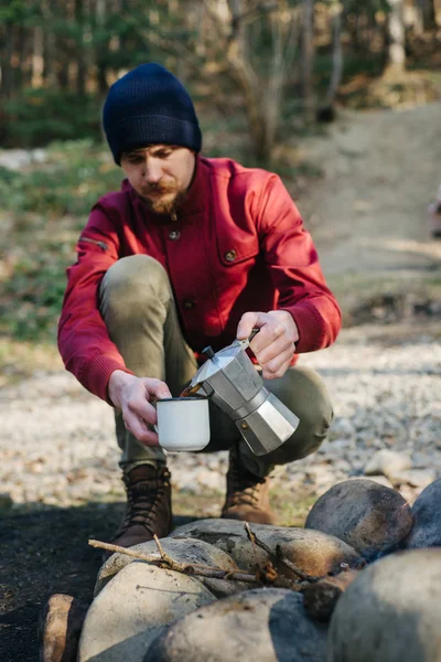 Junger Mann Reisender schenkt Kaffee aus Kaffeemaschine in Metalltasse mit Blick auf erstaunliche Wald, schöne und inspirierende Camp-Lage, hat Mittagessen nach einem langen Spaziergang. Konzept eines gesunden Lebensstils — Stockfoto