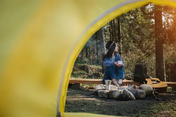 Ηρεμία πυροβόλησε από το εσωτερικό σκηνή κάμπινγκ σε ένα θηλυκό ταξιδιώτη κάθεται κοντά σε φωτιά με θέα καταπληκτική θέα του δάσους, όμορφη και εμπνευσμένη τοποθεσία στρατόπεδο για υπαίθριες δονήσεις τρόπο ζωής — Φωτογραφία Αρχείου