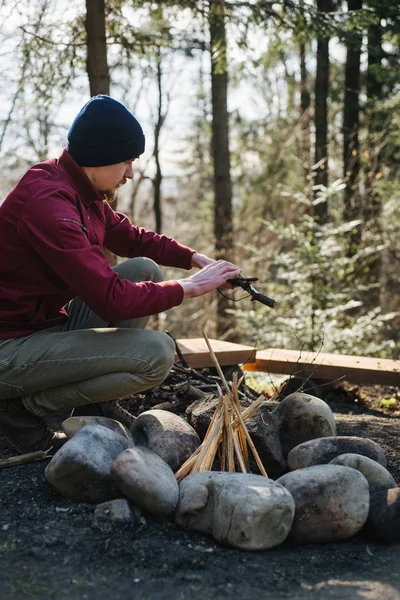 Vertikale Außendarstellung junger Wanderer, die Brunches für das Lagerfeuer im Wald zubereiten. Ein bärtiger Mann, der nach dem Trekking Lagerfeuer macht. Reisen echte Wildnis Lebensstil erkunden — Stockfoto