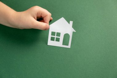 Yeşil arka planda beyaz kağıtlı evi tutan çocuğun en iyi görüntüsü. Aile evi ve emlak konsepti. Düz yat, boşluğu kopyala