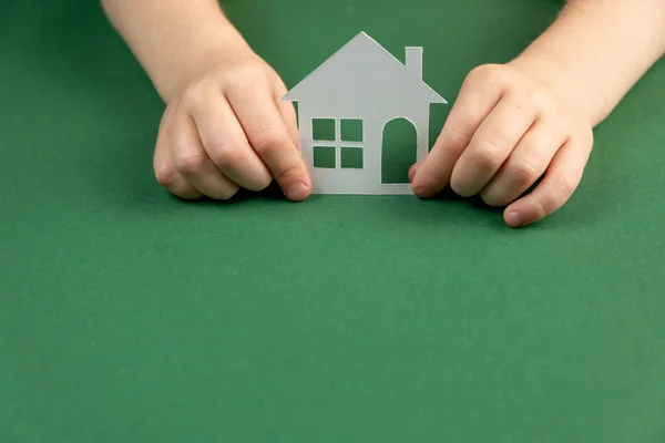 Dakloze opvang en onroerend goed concept. Close-up van kinderhanden met wit papieren huis en hart op groene achtergrond. Vlakke lay, kopieerruimte — Stockfoto