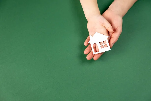 Widok z góry kobiet i dzieci ręce trzymając biały papierowy dom na zielonym tle. Dom rodzinny i koncepcja nieruchomości. Płaskie ułożenie, przestrzeń kopiowania — Zdjęcie stockowe
