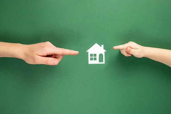 Casa de família e conceito imobiliário. Close up de mãos femininas e infantis segurando casa de papel branco e coração no fundo verde. Flat lay, espaço de cópia — Fotografia de Stock