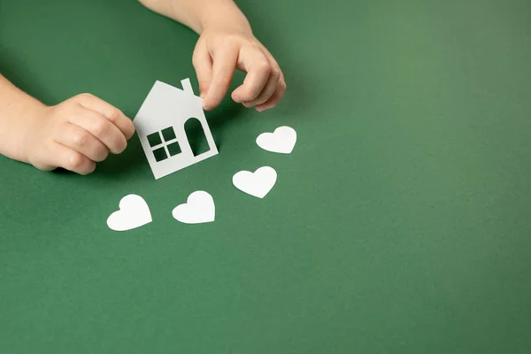 Kinderhände mit weißem Papierhaus und Herz auf grünem Hintergrund. Familienheim und Immobilienkonzept. flache Lage, Kopierraum — Stockfoto
