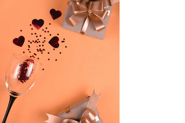 Vakantie achtergrond. Wijnglazen, diverse handgemaakte geschenkdozen versierd met roze hart confetti, wit frame op oranje achtergrond. Valentijnsdag concept. Vlakke lay, bovenaanzicht, kopieerruimte — Stockfoto