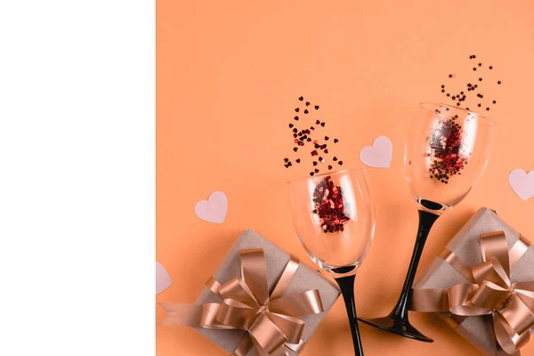 Vakantie achtergrond. Twee klappende wijnglazen, handgemaakte geschenkdozen versierd met roze hart confetti, wit frame op oranje achtergrond. Valentijnsdag concept. Vlakke lay, bovenaanzicht, kopieerruimte — Stockfoto