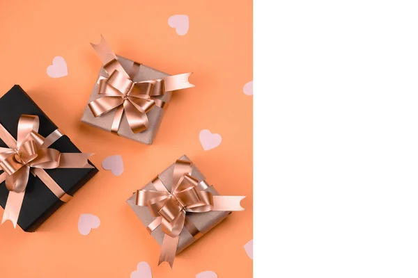 Holiday background. Various handmade gift boxes decorated with pink heart confetti, white frame on orange background. Minimal style and valentines day concept. Flat lay, top view, copy space — ストック写真