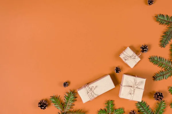 Noel ya da kış kompozisyonu. Köknar ağacı dallarından, çam ağacından ve pastel turuncu arka planda el yapımı hediye kutularından yapılmış çerçeve. Noel, kış, yeni yıl konsepti. Düz konum, üst görünüm, kopyalama alanı — Stok fotoğraf