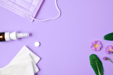 Alerji konsepti. Mendil, hap, yüz maskesi, şişe ve çiçeklerin mor arka planda olduğu sezonluk bahar ve yaz polen alerjisi gibi yaratıcı düz konsept. Üst görünüm, alanı kopyala