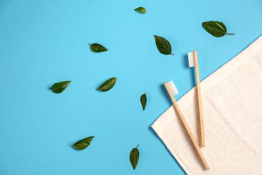 İki ahşap bambu çevre dostu diş fırçası, yeşil yaprak, mavi arka planda beyaz havlu. Çevre dostu, yeniden kullanım ve sevgililer günü konsepti. Düz konum, üst görünüm, kopyalama alanı