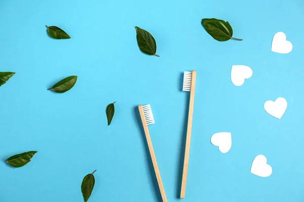 Zero waste concept. Two wooden bamboo eco friendly toothbrushes, green leaf, white hearts on blue background. Eco friendly, valentines day concept. Flat lay, copy space — Stock Photo, Image