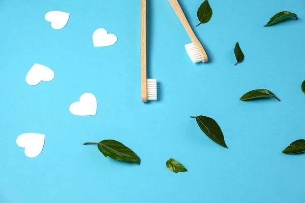 Zero conceito de desperdício. Duas escovas de dentes eco friendly de bambu de madeira, folha verde, corações brancos no fundo azul. Eco amigável, conceito dia dos namorados. Flat lay, espaço de cópia — Fotografia de Stock