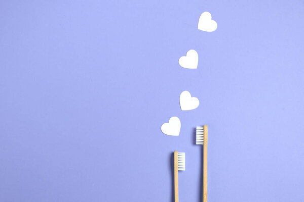 Zero waste concept. Two wooden bamboo eco friendly toothbrushes, white hearts on purple background. Eco friendly, valentines day concept. Flat lay, copy space