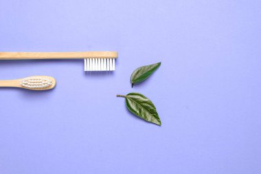 İki ahşap bambu çevre dostu diş fırçası ve mor arka planda yeşil yaprak. Diş bakımı ve sıfır atık konsepti. Düz konum, üst görünüm, kopyalama alanı