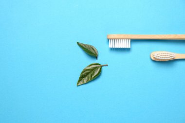 Sıfır kayıp. İki ahşap bambu çevre dostu diş fırçası ve mavi arka planda yeşil yaprak. Diş bakımı, çevre dostu ve yeniden kullanım konsepti. Düz konum, üst görünüm, kopyalama alanı
