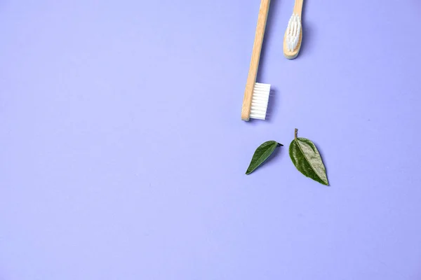 Duas escovas de dentes ecológicas de bambu de madeira e folha verde no fundo roxo. Cuidados dentários e zero conceito de desperdício. Flat lay, vista superior, espaço de cópia — Fotografia de Stock